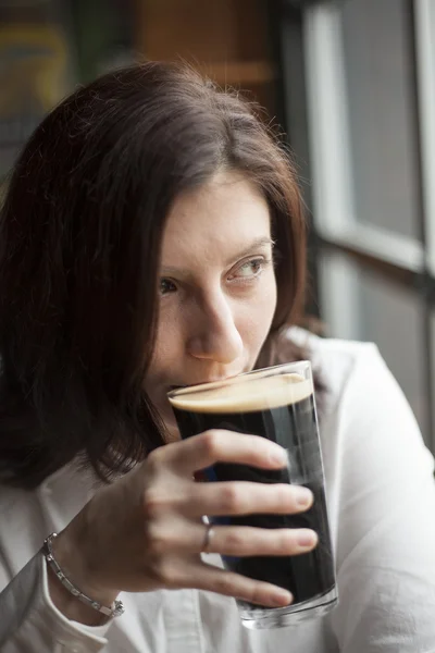 Mulher jovem com belos olhos castanhos bebendo uma caneca de Stout — Fotografia de Stock