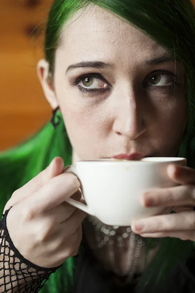 Молодая женщина с красивыми зелеными волосами и глазами пьет кофе — стоковое фото