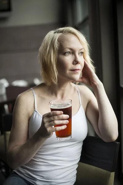 Blonde vrouw met mooie blauwe ogen drinken glazen van pale ale — Stockfoto