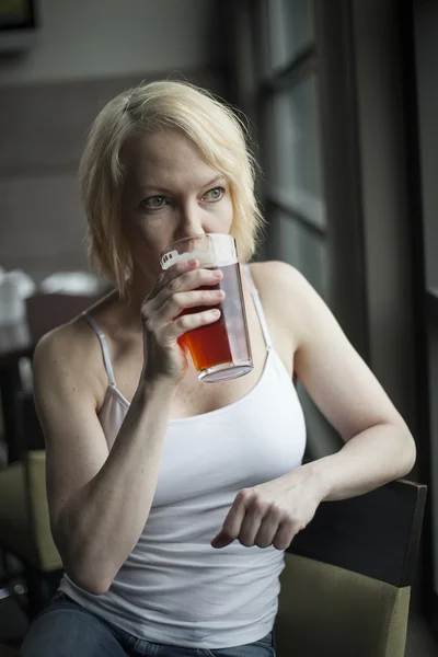 Blonde Frau mit schönen blauen Augen trinkt Glas mit blassem Ale — Stockfoto