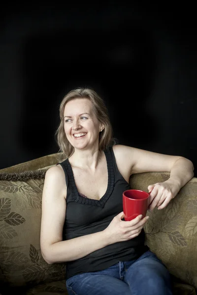 Rire femme blonde avec tasse de café rouge sur fond noir — Photo