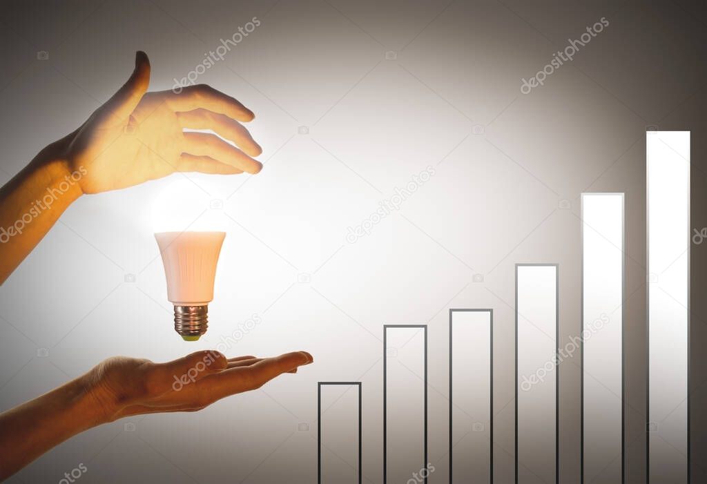 Hand holding light bulb.The concept of eco-energy, innovation. Growth chart with hands illuminated by LED light bulb.