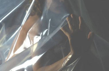 Karanlık arka planda polietilen kaplı çıplak bir kadın. Ekoloji ve plastik kirliliği kavramı.