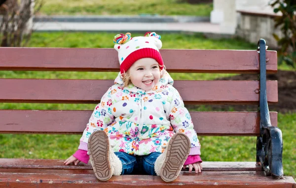 Счастливая девочка, сидящая на скамейке — стоковое фото
