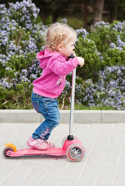 Barn girl på en skoter i en park — Stockfoto