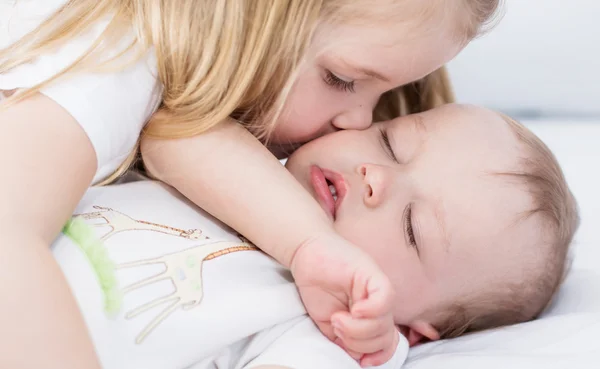 Little girl kisses a sleeping baby brother — Stock Photo, Image