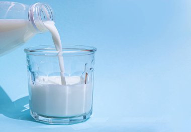 Süt açık mavi arkaplanda bir bardağa dökülür..
