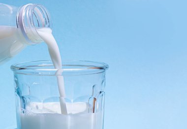 Süt açık mavi arkaplanda bir bardağa dökülür..