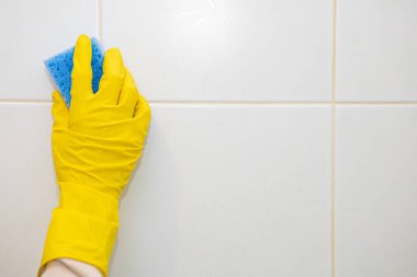 Sarı lastik eldivenli eller banyodaki fayansları yıkıyor..