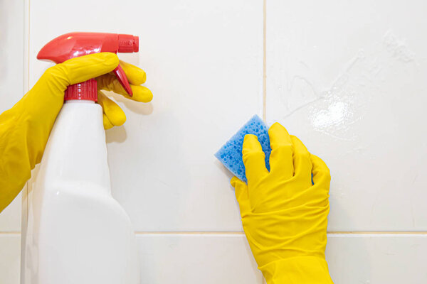 Hands in yellow rubber gloves washing the tiles in the bathroom.