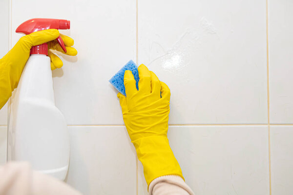 Hands in yellow rubber gloves washing the tiles in the bathroom.