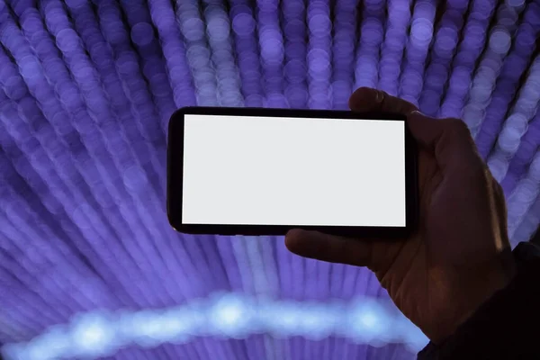 Cep telefonlu el, gece bulanık arka planda Noel ışıklarının fotoğrafını çeker. Yeni yıl modeli, tatil konsepti, kutlama ve kış yürüyüşleri.