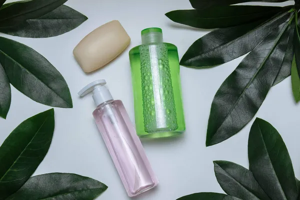Beyaz arka planda yeşil bambu yapraklı plastik tonik ve jel şişeleri ve sabun. Üst manzara yazı, cilt bakımı konsepti, kozmetik, makyaj, ürün reklamı, kaplıca için boş alan.
