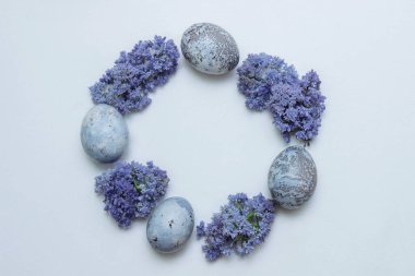Round frame with wreath of Easter eggs painted in blue purple lilac and muscari flowers on white background with empty space for text, copy space, closeup, greeting card design concept, spring holiday