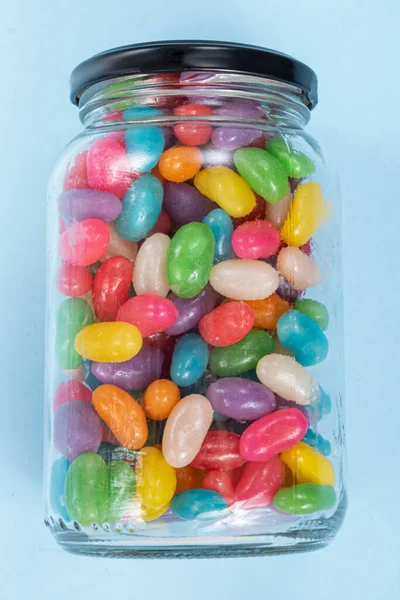 Several Jelly Beans on the blue background inside the glass pot