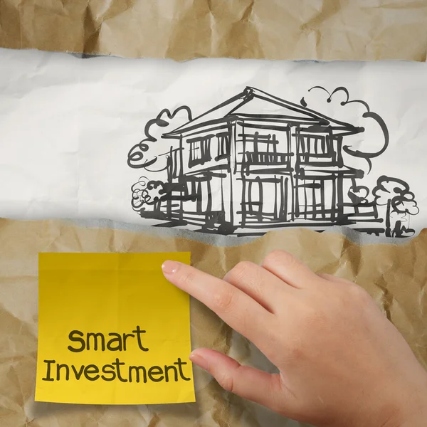 Mão segurando nota pegajosa de investimento inteligente com casa em rugas — Fotografia de Stock