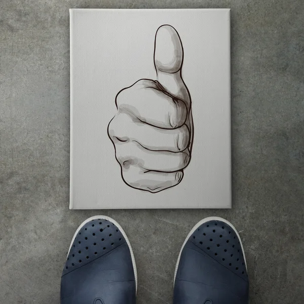 Hand giving a thumbs up on front of business man feet as concept — Stock Photo, Image