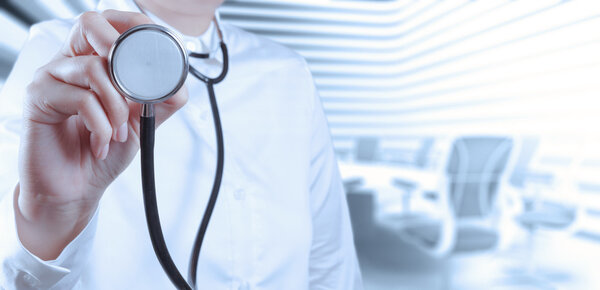 Врач со стетоскопом в руках и на рабочем фоне
 