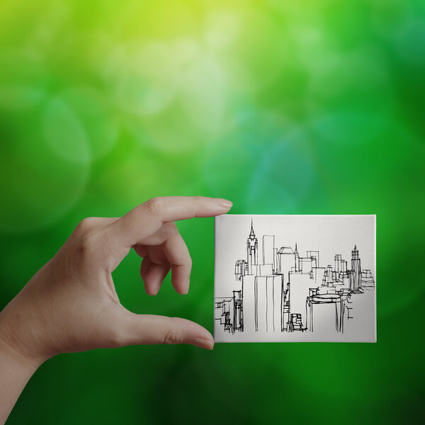 hand showing hand drawn city on canvas board on green nature bac