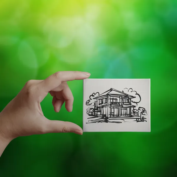 Hand holding hand drawn house on canvas board on green backgroun — Stock Photo, Image