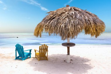 Tropikal bir kumsalda saman şemsiyesi ve renkli sandalyeler.