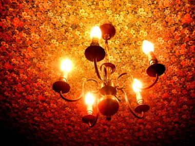 Vintage brass light fitting suspended from a kitchen ceiling where the walls and ceiling are covered in flowery wallpaper in the French style