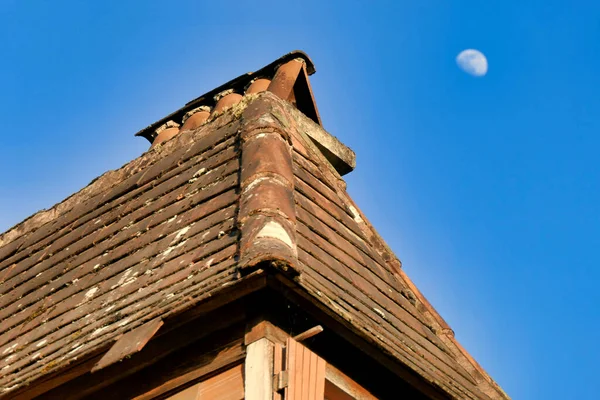 Old roof on a dormer window of a 200 year old French farmhouse in a state of disrepair with loose, broken and missing tiles. Moon in the background