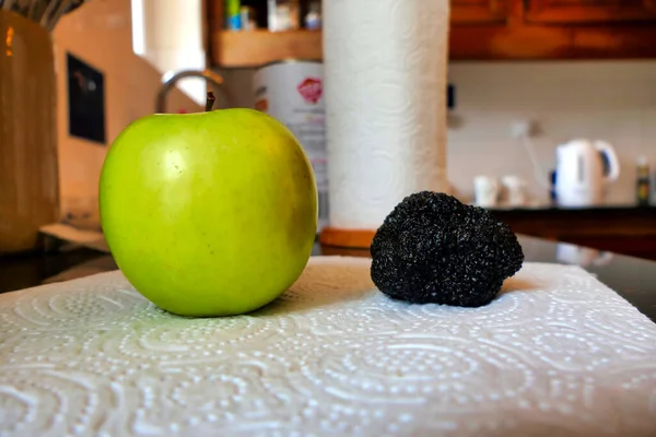 A large Perigord truffle, known as the black diamond, next to an apple to give an indication of size
