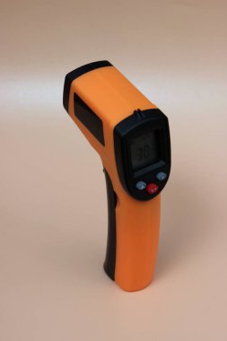 Sarı zemin üzerindeki sıcaklığı ölçmek için kızılötesi termometre (termometre). Covid-19 yayılma önleme kavramı. 