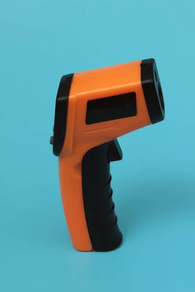 Infrared thermometer (thermometer gun) for measuring temperature over blue background. Covid-19 spread prevention concept.
