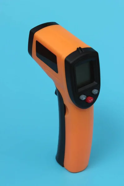 Infrared thermometer (thermometer gun) for measuring temperature over blue background. Covid-19 spread prevention concept.