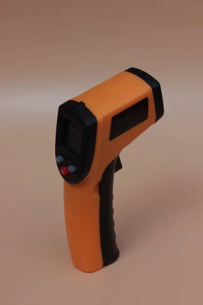 Infrared thermometer (thermometer gun) for measuring temperature over yellow background. Covid-19 spread prevention concept.
