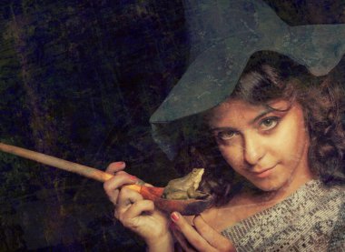 Cadı şapkalı güzel kız kara arka planda kurbağayla poz veriyor.