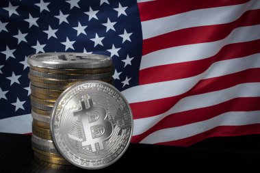 Bir gümüş bitcoin ve ABD bayrağı üzerinde bitcoin yığını