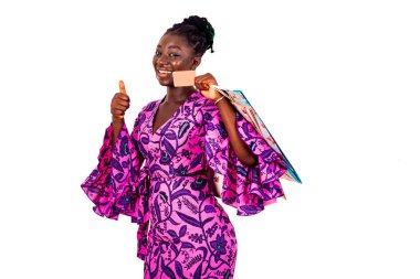 Geleneksel peştemalli genç ve güzel bir iş kadını. Elinde kredi kartı ve alışveriş poşetleri tutarken baş parmağını gösteriyor..