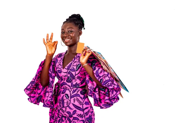 Geleneksel peştemalli genç bir iş kadını parmaklarıyla, kredi kartıyla ve alışveriş torbalarıyla gülümseyerek iyi bir jest yapıyor..