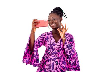 Güzel genç iş kadını cep telefonuyla fotoğraf çekiyor. Parmaklarıyla gülümseyerek iyi bir hareket yapıyor..