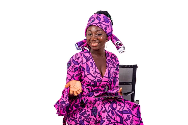 Geleneksel peştamallı güzel bir iş kadınının portresi sandalyeye oturmuş, elinde dijital tablet tutarken gülümsüyor..