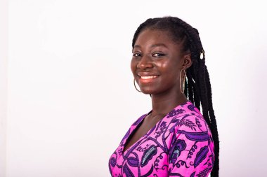 Saçları beyaz arka planda dikilmiş, gülümseyen kameraya bakan güzel Afrikalı kadın..