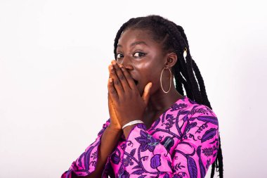 Beyaz arka planda örgü ören güzel Afrikalı bir kadın elleri ağzında şaşırmış bir şeye bakıyor..