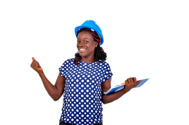 Güzel genç bayan inşaat mühendisi elinde bir pano tutarken ve başparmağını geriye uzatırken gülümsüyor..