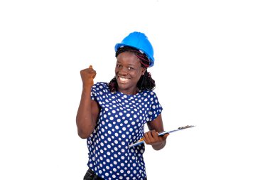 Güzel genç bayan inşaat mühendisi elinde bir pano tutarken ve başparmağını geriye uzatırken gülümsüyor..