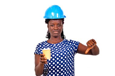 Güzel bayan inşaat mühendisi mavi kasklı, elinde kağıt kahve fincanı tutan ve baş parmağını aşağı gösteren..