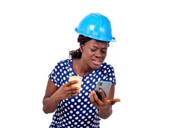 Genç bayan inşaat mühendisi mavi bir şapka takıyor elinde bir fincan kahve ve cep telefonu kullanıyor..