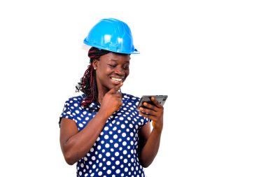 Genç bayan mühendis mavi güvenlik kaskı takıyor ve gülümserken cep telefonundan video izliyor..