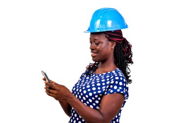 Güvenlik kasklı güzel bir kadın mühendis beyaz arka planda duruyor cep telefonundan mesaj okuyor, gülümsüyor..