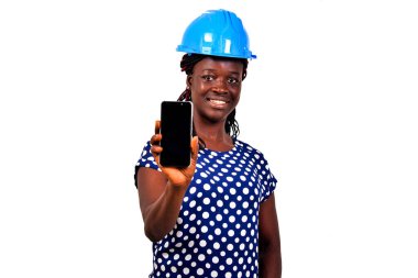Güvenlik kasklı güzel bir bayan mühendis beyaz arka planda duruyor cep telefonunu sunuyor, gülümsüyor..