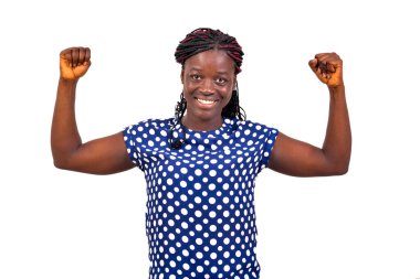 Güzel, genç ve mutlu bir kadının portresi beyaz arka planda duruyor ve kollarını kaldırarak gülümseyerek zafer jesti yapıyor..