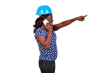 Güvenlik kaskı olan güzel bir kadın mühendis beyaz arka planda duruyor cep telefonuyla konuşuyor ve gülümsüyor..