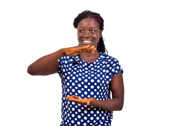 Güzel, mutlu genç bir kadının portresi beyaz arka planda duruyor ve elleriyle gülümseyerek bir şeyler gösteriyor..